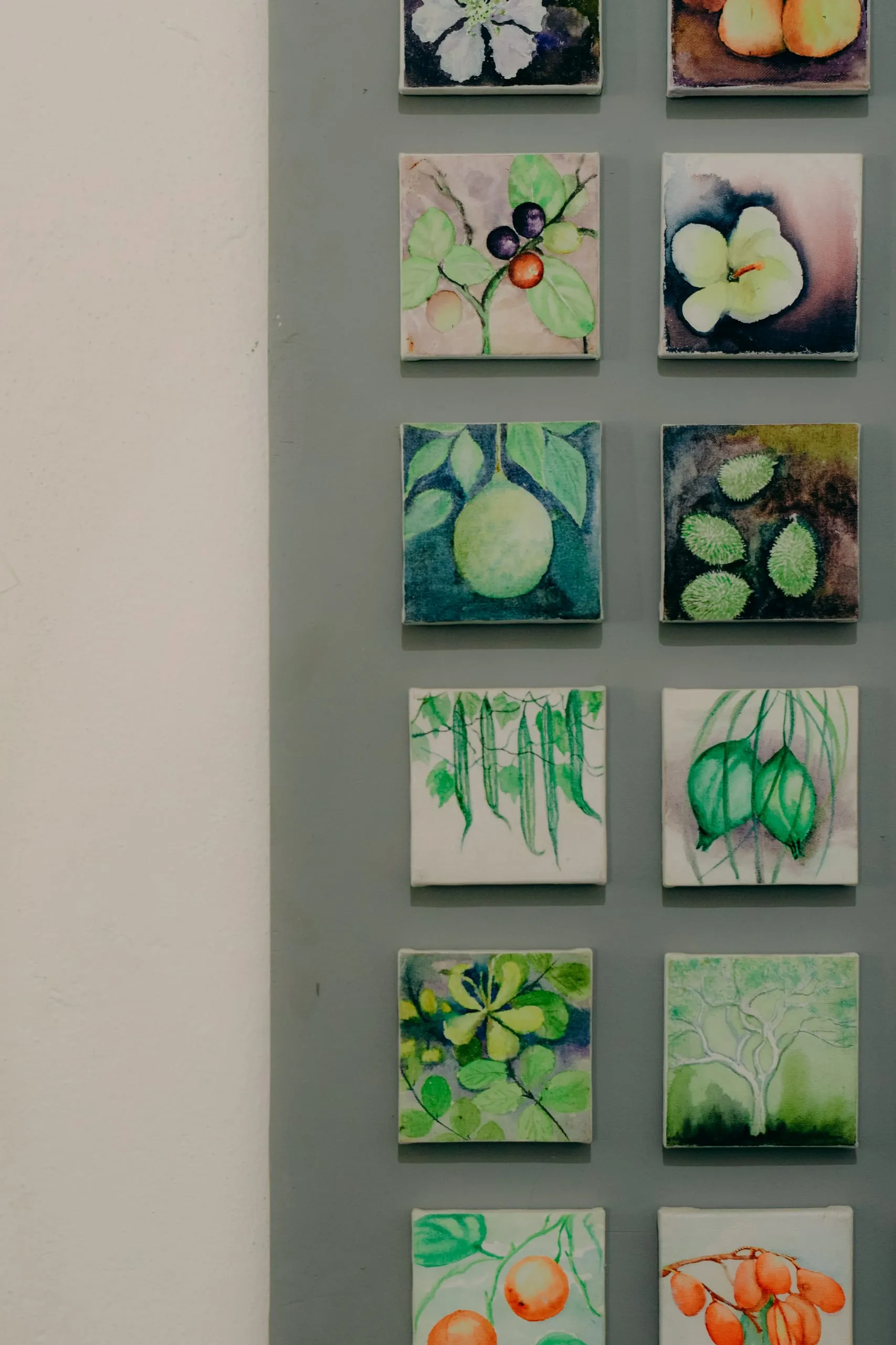 A grid of small painted botanical tiles on a grey-green wall