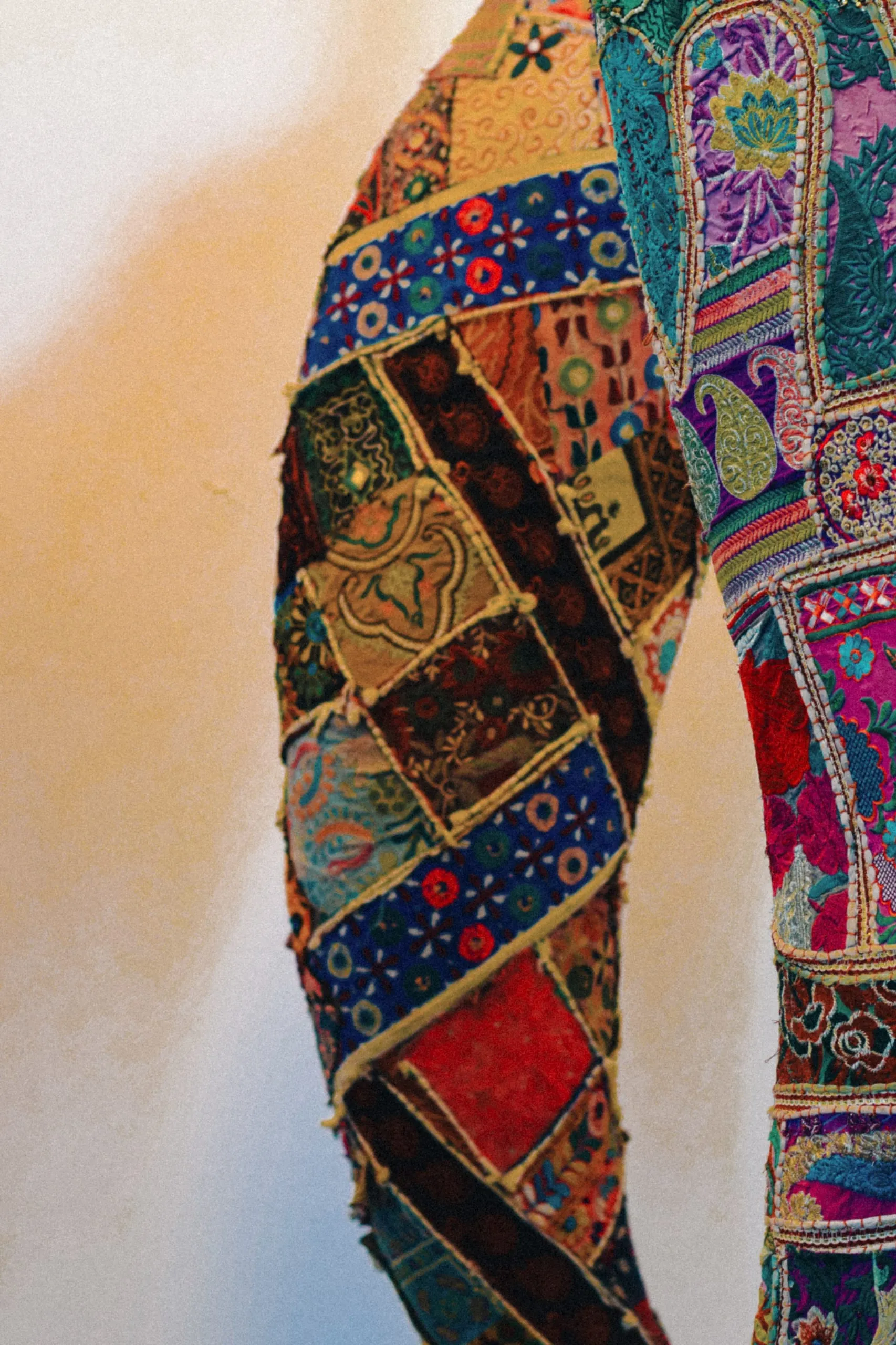 A colourful patchwork textile shaped like an elephant's trunk, against a warm wall