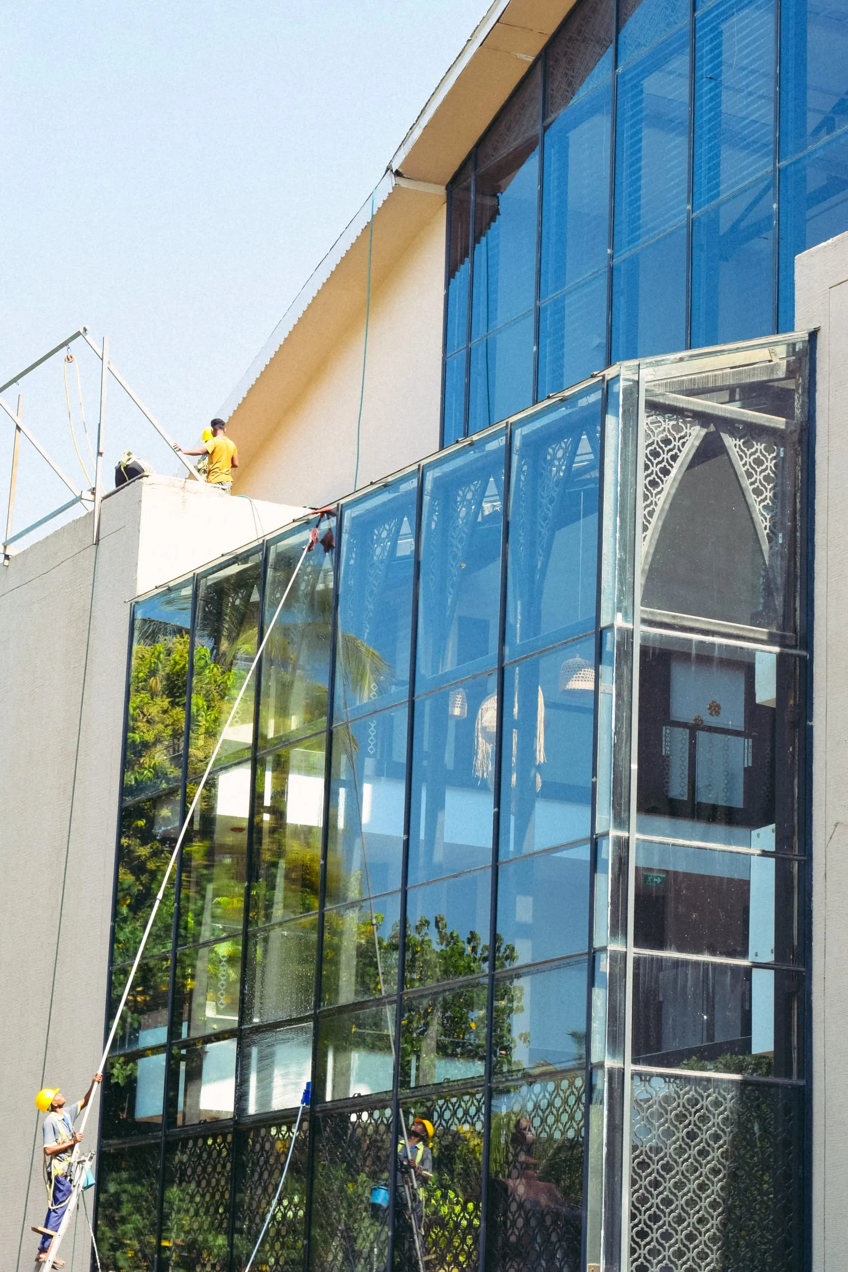 Workers on ropes cleaning the tall glass front of a white building